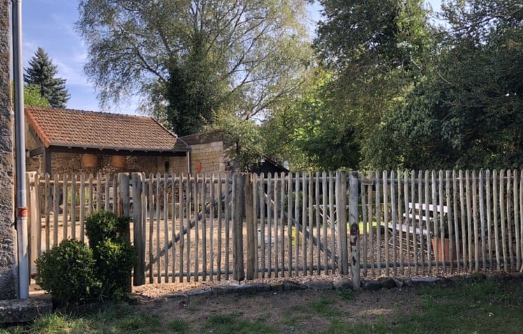 Dubbele franse rondhoutpoort van 120 cm breed bij 120 cm hoog per poortdeel bevestigd aan hekwerk van kastanjehouten palen en halfronde rasterlatten als doorgang naar de oprit bij een huis.