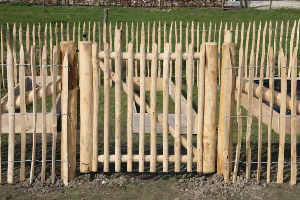 Franse rondhoutpoort van kastanjehout van 100 cm hoog en 100 cm breed als doorgang naar een moestuin met schapenhek van 100 cm hoog als omheining.