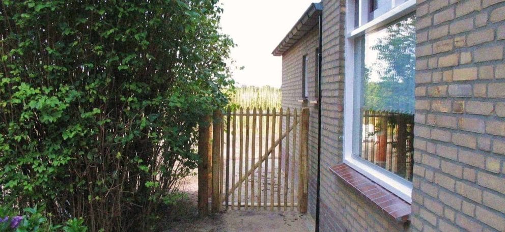 Franse rondhoutpoort van 120 cm hoogals doorgang tussen een woning en een heg