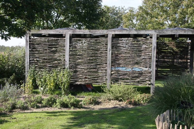 Hazelaarscherm Somme 1 gebruikt als creatieve afrastering in een tuin. De schermen zijn geplaatst tussen een houten balken constructie.