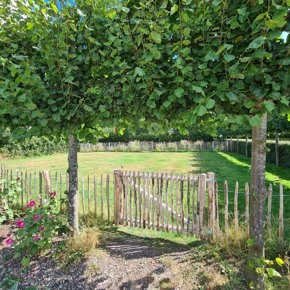 Franse rondhoutpoort van 100 cm hoog en 150 cm breed als toegang naar een weide in de tuin.