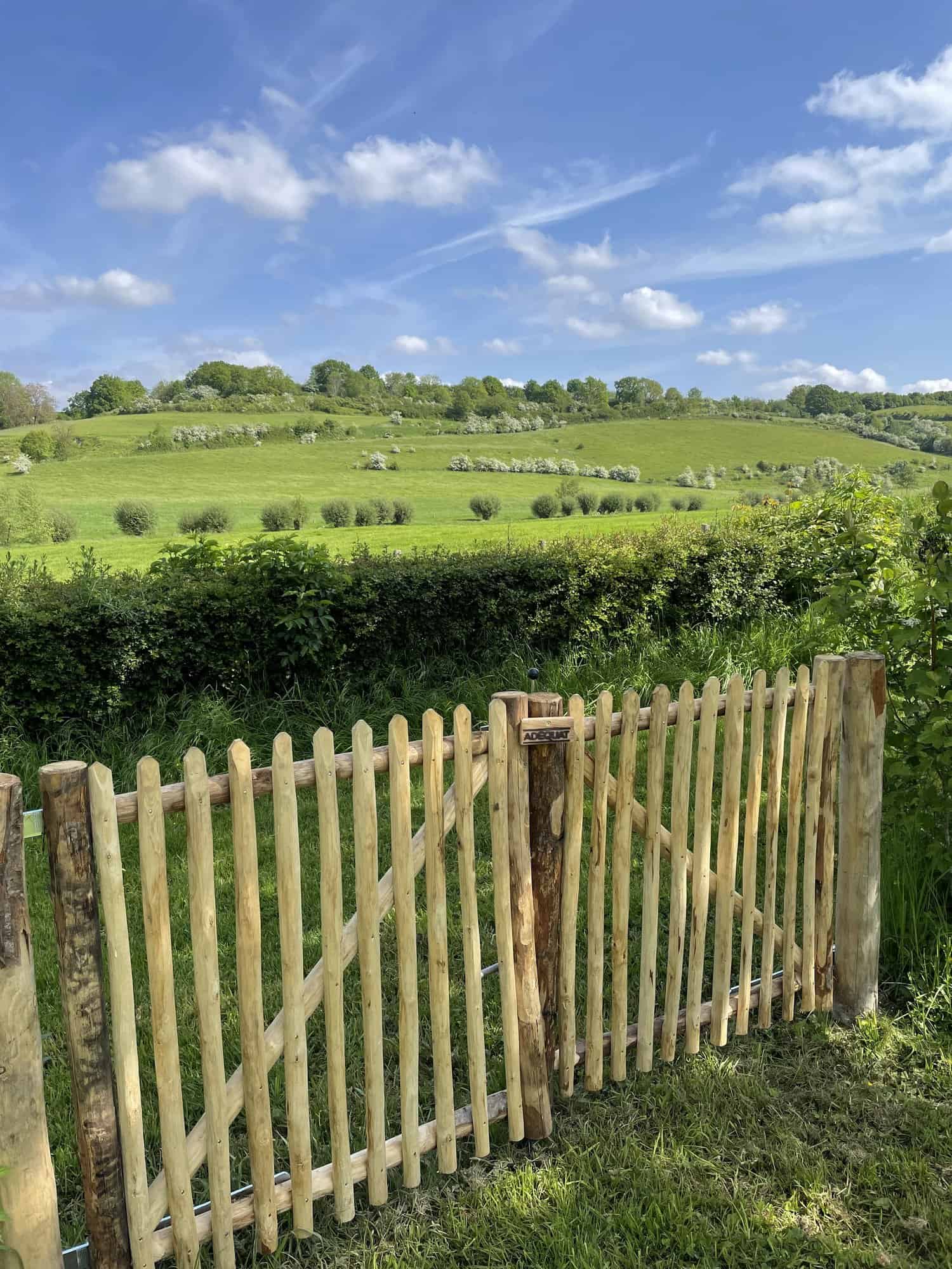 Dubbele franse rondhoutpoort van 100 cm breed en 100 cm hoog met een simpele sluiting aan de buitenkant. De foto is genomen vanaf de voorkant van de poort en je kijkt uit over een mooi groen landschap.