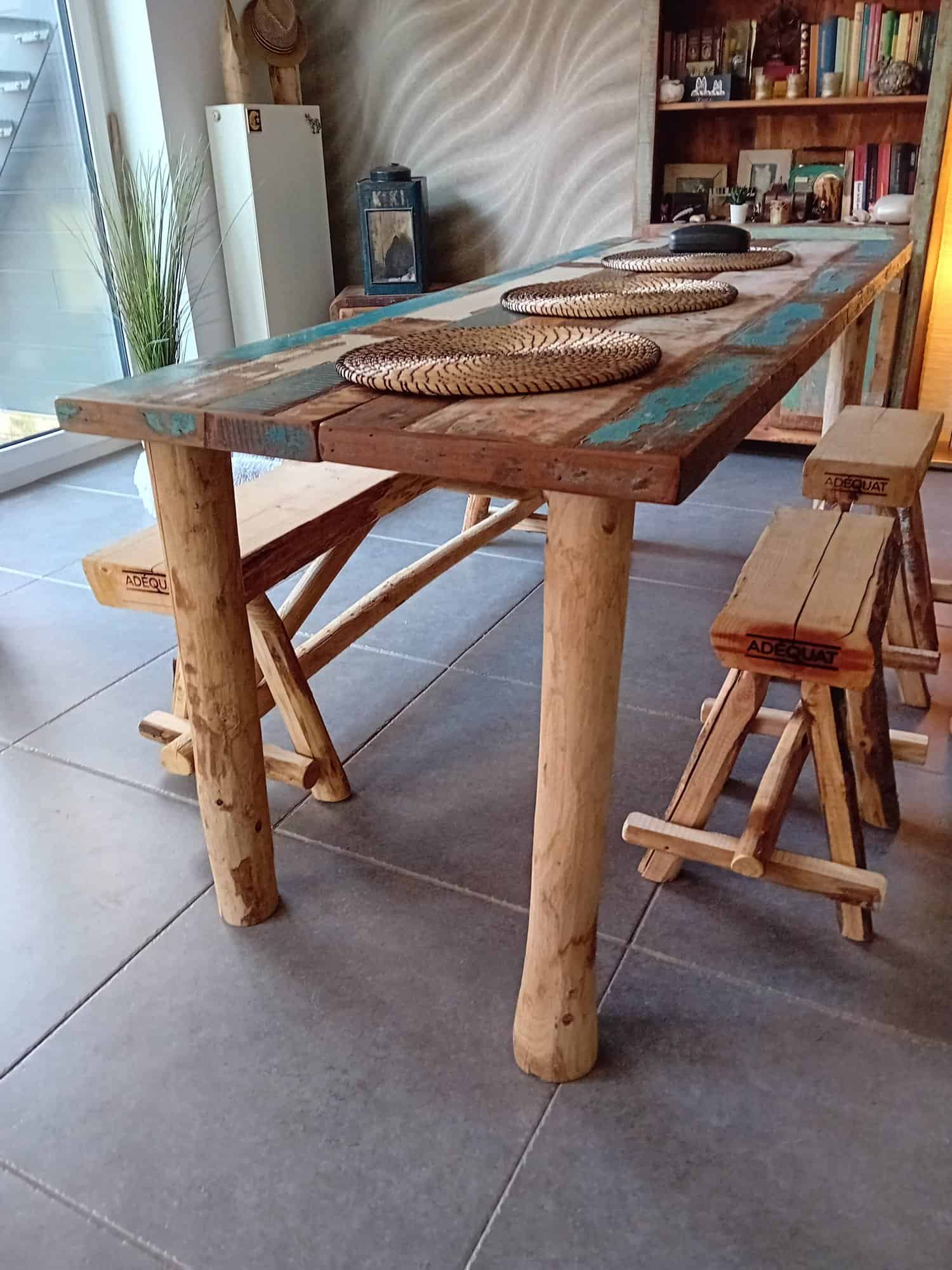 Boomstamkankje van kastanjehout van 150 cm breed en twee kastanjehouten krukjes. Deze staan bij een tafel binnen in de woning. De bankjes en de tafel stralen een Ibiza look uit.